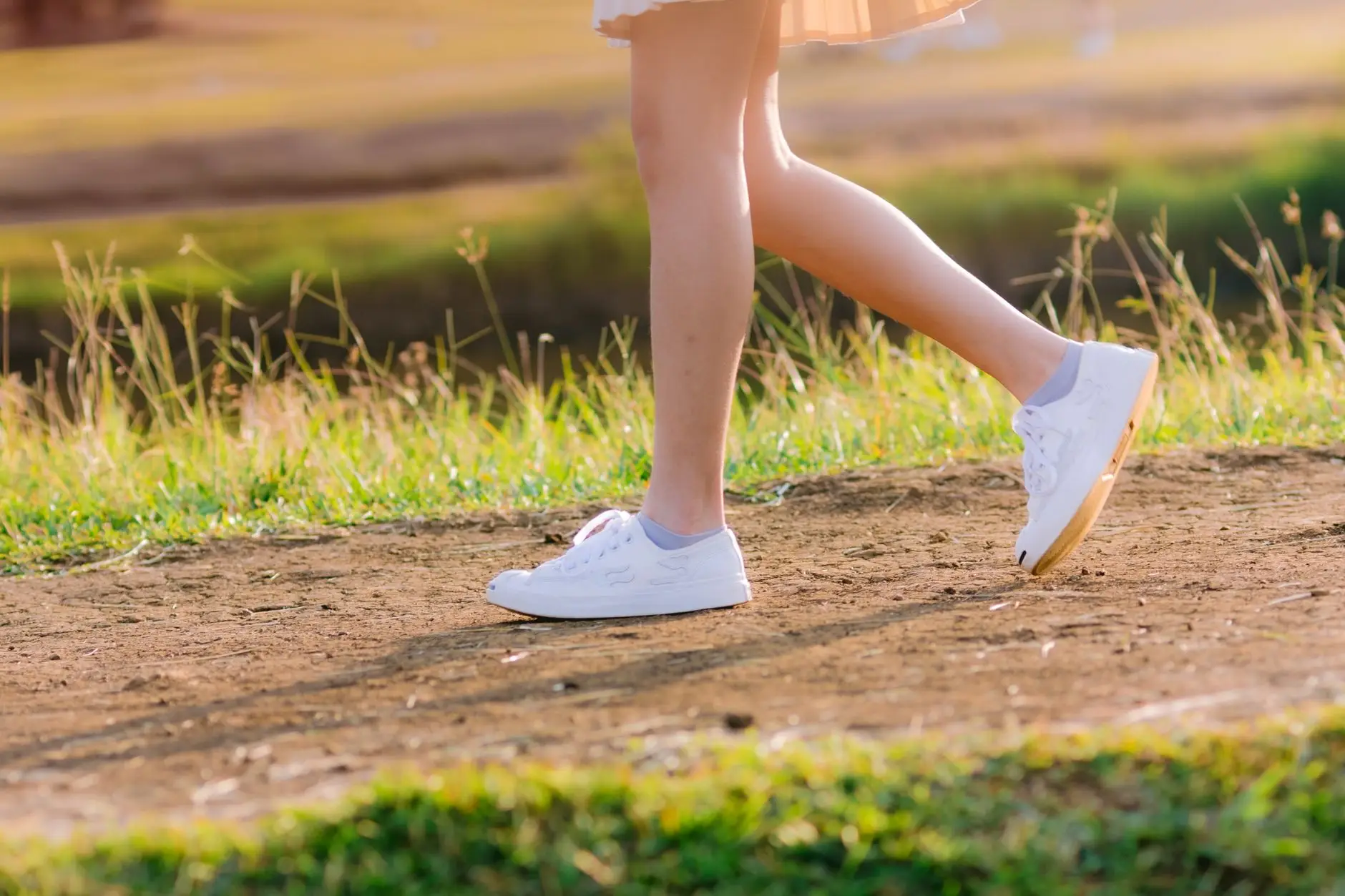 woman walking on dirt path in sunlit park
